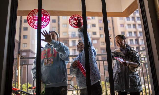 Členové rodiny nalepují ve svém novém domě papírové ozdoby, aby uvítali první čínský nový rok poté, co se vymanili z chudoby v okrese Huize (Chuej-ce) v Qujingu (Čchü-ťin-ku) v provincii Yunnan (Jün-nan) v jihozápadní Číně, 11. února 2021. (Xinhua / Jiang Wenyao)