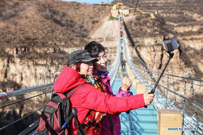 Des touristes marchent sur un pont suspendu en verre dans le site touristique de Hongyagu à Pingshan, district de la province chinoise du Hebei (nord), le 24 décembre 2017. Le pont suspendu en verre, d'une longueur de 488 mètres, a officiellement ouvert au public dimanche. (Xinhua/Liu Peiran)