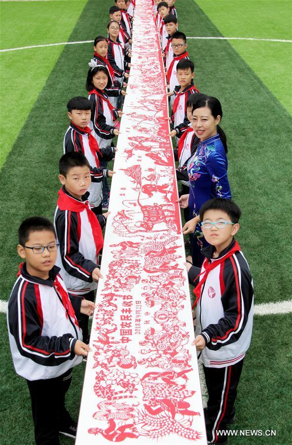  L'artiste spécialiste du papier découpé, Qiu Ting, et son mari Qiu Hanping, regardent une oeuvre sur le thème de la récolte chez eux, à Tengzhou, ville de la province chinoise du Shandong (est), le 17 septembre 2018. Mme Qiu a passé plus de deux mois pour créer cette oeuvre en papier découpé d'une longueur de 2.018 centimètres à l'approche de la première fête de la récolte des agriculteurs chinois, qui tombera pendant l'équinoxe d'automne, soit le 23 septembre prochain. (Photo : Song Haicun)