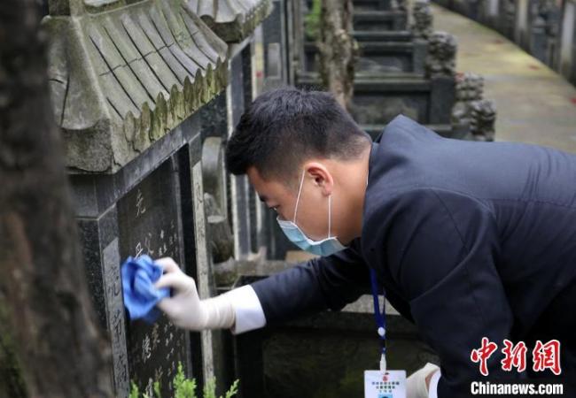 Des employés du cimetière offrent des fleurs et nettoient une tombe à la place de ses clients, le 29 mars, à Liuzhou, dans la province du Guangxi.