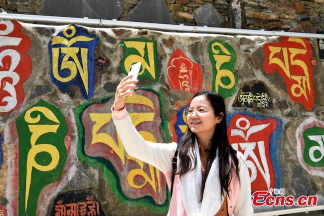 Μια τουρίστρια παίρνει μια selfie μπροστά από έναν πέτρινο σκαλιστό τοίχο σε ένα πάρκο πετρογλυφικών στο Μπανγκτουό, κομητεία Ρανγκτανγκ του Αυτόνομου Νομού Θιβετιανών Νγκάγουα (Άμπα) και Τσιανγκ στην επαρχία Σιτσουάν της νοτιοδυτικής Κίνας, στις 13 Ιουνίου 2020.