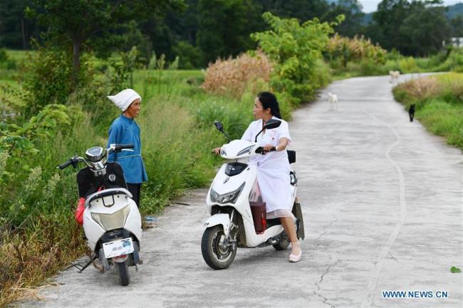 Η Λουό Μου συνομιλεί με έναν χωρικό δρόμο στο δρόμο πηγαίνοντας να επισκεφθεί έναν ασθενή στο χωριό Τσουιγουέι της κομητείας Λονγκλί, στην αυτόνομη περιφέρεια Τσιενάν Μπουγί-Μιάο στην επαρχία Γκουιτζόου της νοτιοδυτικής Κίνας, 18 Αυγούστου 2020.