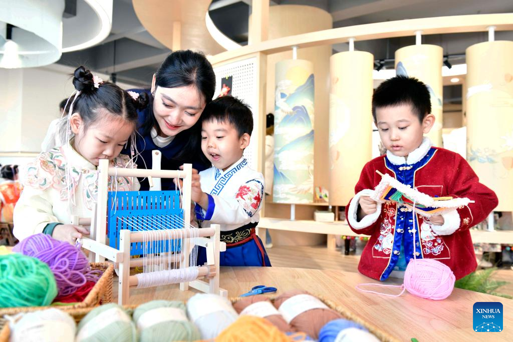 Η δασκάλα Χου Χουϊσίν διδάσκει στα παιδιά να πλέκουν και να υφαίνουν στο νηπιαγωγείο Σανγουάνγκ στο Τζινάν, στην επαρχία Σανντόνγκ της ανατολικής Κίνας, στις 29 Νοεμβρίου 2023. (Xinhua/Guo Xulei)