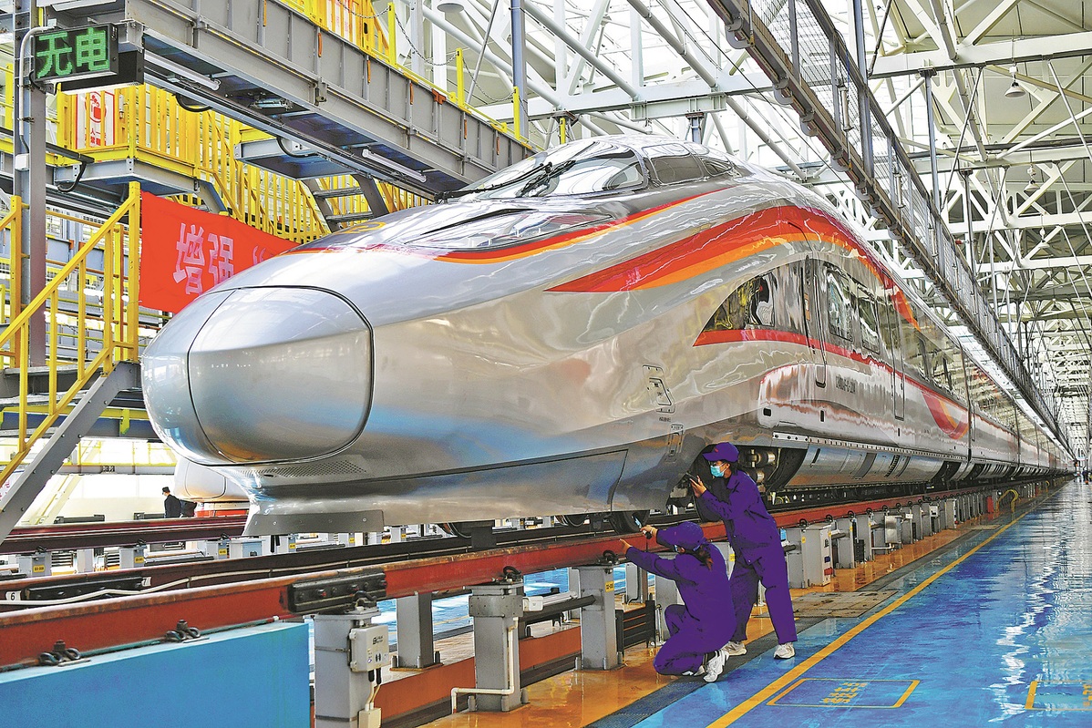 Οι εργαζόμενοι συντήρησης ελέγχουν ένα τρένο-σφαίρα Φουσίνγκ σε μια αποθήκη στο Σιονγκ’αν στις 27 Δεκεμβρίου 2021. [Φωτογραφία από τον Sun Lijun/For China Daily]