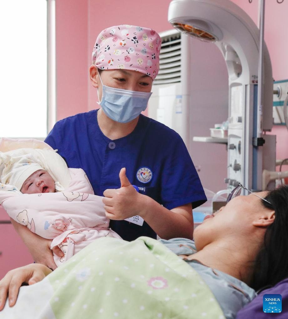 Μια νοσοκόμα κρατά ένα νεογέννητο μωρό ενώ μιλά με τη μητέρα σε ένα νοσοκομείο στην πόλη Σουτζόου, στην επαρχία Τζιανγκσού της ανατολικής Κίνας, 12 Μαΐου 2024. (Φωτογραφία Bai Xue/Xinhua)